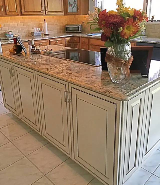 A kitchen island with granite countertop, featuring a sink, a flower vase, and wooden cabinets.