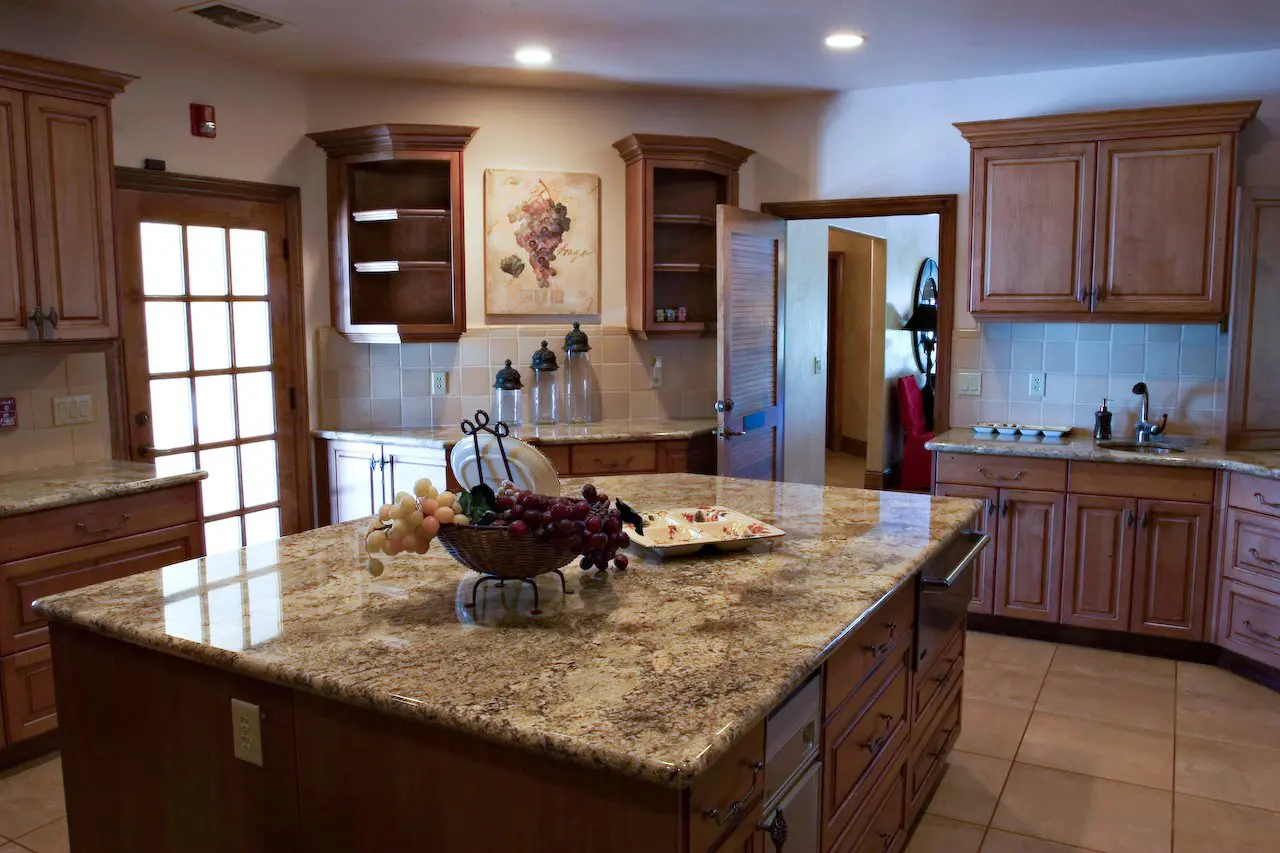 A spacious kitchen with wooden cabinets, granite countertops, and a fruit bowl on the island.
