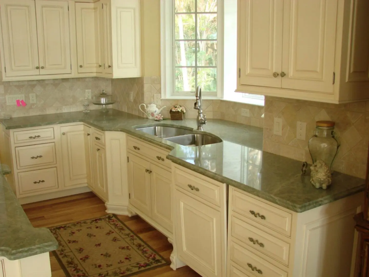 A bright kitchen interior with beige cabinetry and green granite countertops.