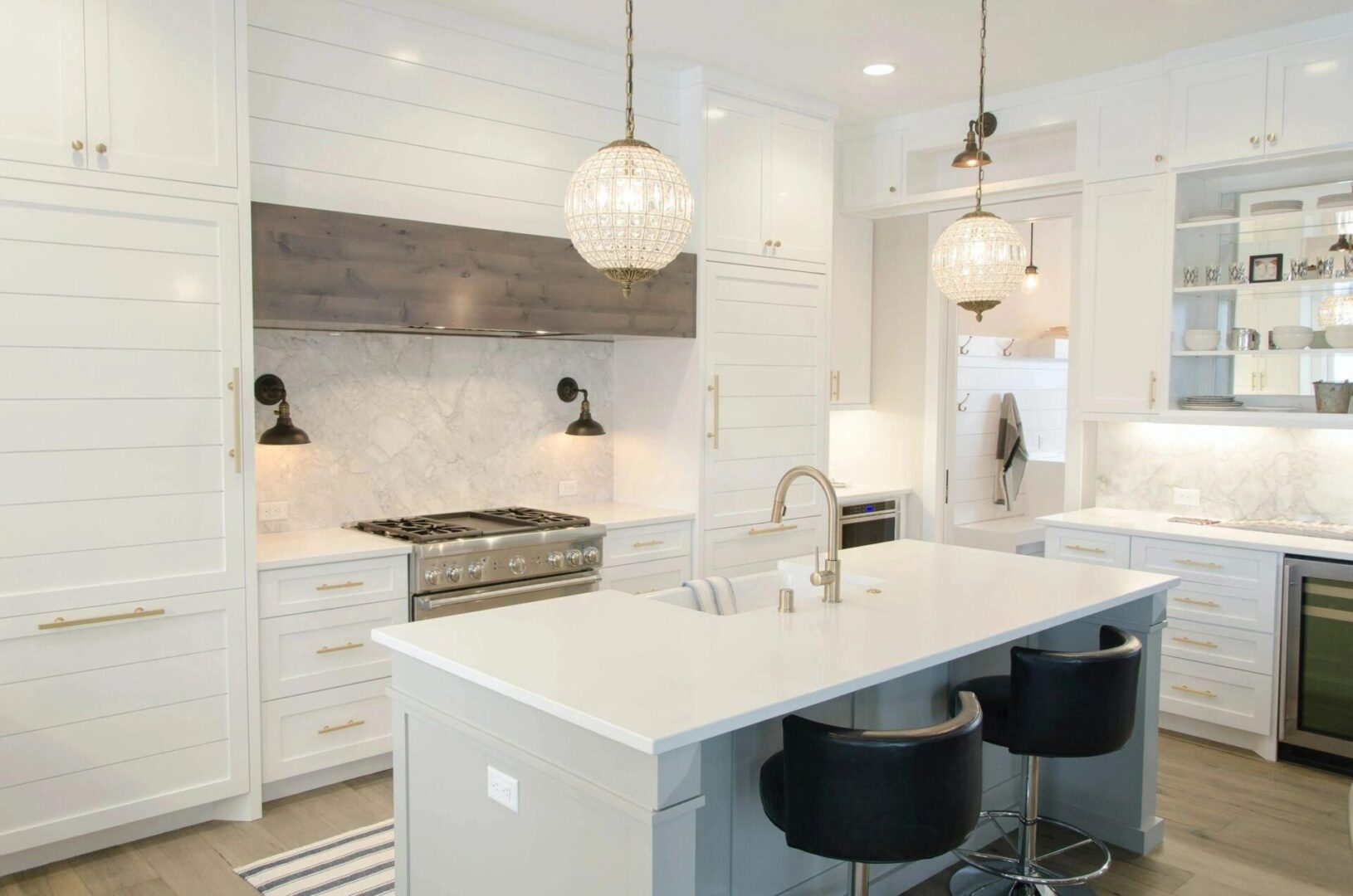 Modern kitchen interior with white cabinetry, marble countertops, and hanging pendant lights over a central island with bar stools.